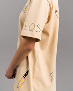 Seitenansicht des T-Shirts mit Schriftzug „LOST“ auf dem rechten Ärmel. Darunter ein Messer mit Blumen sowie eine kleine, gebogene Sense. Auf der Schulter ist ein rosa Feuerzeug aufgedruckt.