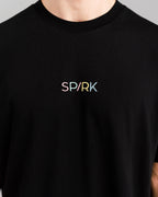 Detailansicht des bunten, mittig platzierten Schriftzugs „SPARK“ auf der Brust des schwarzen Shirts.