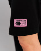 Nahaufnahme des pinken Labels mit schwarzem SPARK-Code am linken Ärmel des schwarzen Shirts.