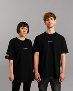 Zwei Personen tragen das schwarze SPARK-T-Shirt mit farbigem Logo und Label am linken Ärmel, locker geschnitten.