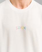 Nahaufnahme der farbigen „SP/RK“-Stickerei auf dem weißen T-Shirt. Die Buchstaben sind in Rosa, Mint, Gelb und Blau gestickt.