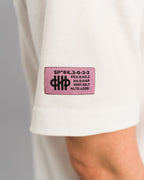 Linker Ärmel des weißen T-Shirts mit aufgenähtem pinkfarbenem Label, bedruckt mit schwarzen Symbolen und codiertem Text.