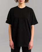 Schwarzes Oversized-T-Shirt mit schwarzer SP/RK-Stickerei auf der Brust, getragen von einer Person in Frontalansicht.