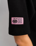 Detailansicht des pinken Labelpatches am linken Ärmel mit schwarzer Typografie und Symbolgrafik.