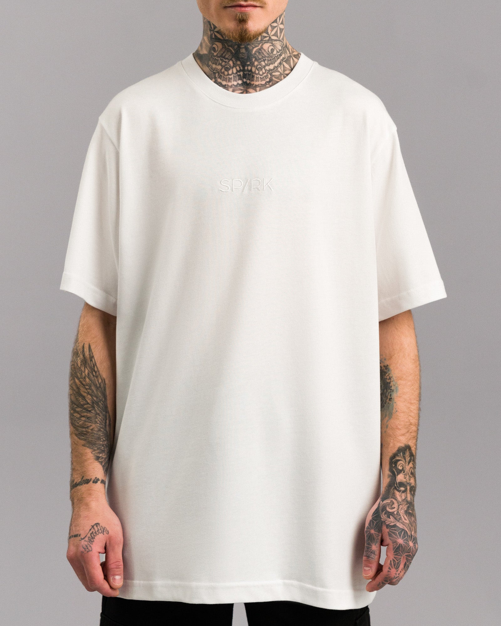 Vorderansicht eines weißen T-Shirts mit dezentem, weiß gesticktem „SPARK“-Schriftzug auf der Brust. Das Shirt hat einen klassischen Rundhalsausschnitt und ist locker geschnitten.