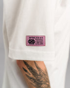 Detailaufnahme des linken Ärmels mit pinkfarbenem, eckigem Label mit schwarzem Text und Logo auf dem weißen Stoff.